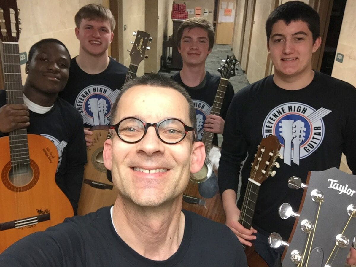 guitar teacher taking a selfie with guitar students in background