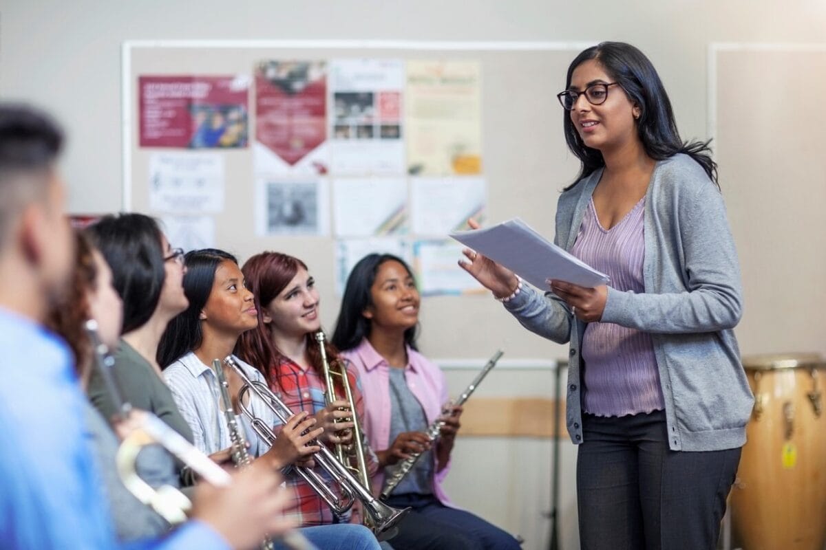 Smiling Indian female tutor with students in music band class