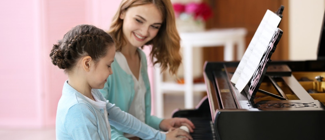 Female teacher teaching piano lessons sitting next to her young female student.