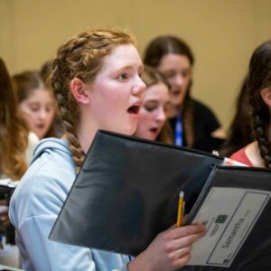 Young girl singing with her all female choir holding a music book.