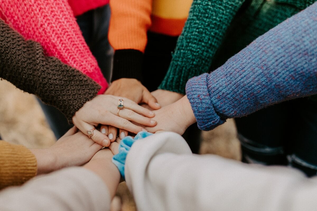 hands from people of diverse backgrounds with multicolored sleeves joined in a circle