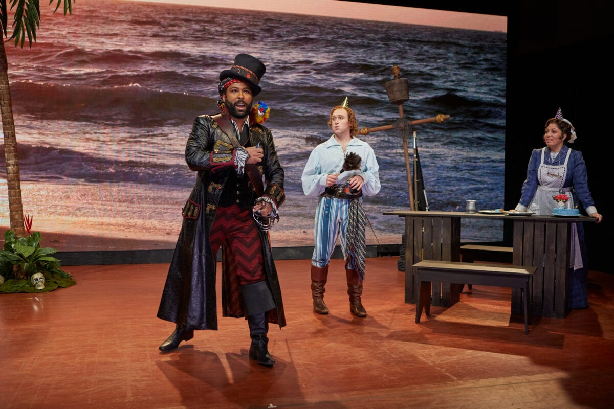 scene from Pirates of Penzance from Opera Theatre of Saint Louis with a man featured singer in foreground and ship scene and two other cast members in background