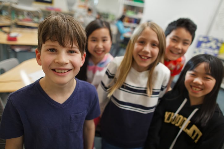 Portrait of multiracial elementary school students boys and girls in classroom together smiling