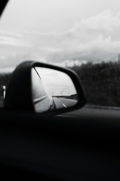 black and white photo showing reflection in a sideview mirror behind where you're going