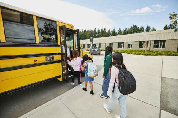Wide shot middle school students boarding school bus for commute home