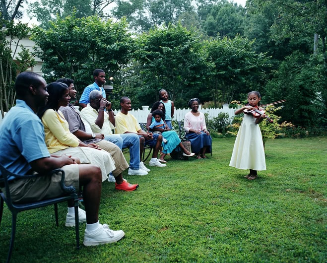 Family watching girl playing violin in yard, side view