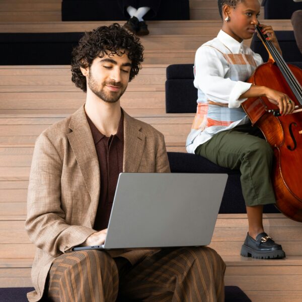 man on laptop in concert hall with woman playing cello