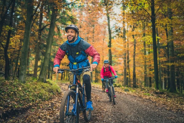 Smiling young Black man riding bike with a friend outdoors in autumn