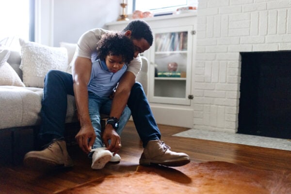 Father helps his son tie a shoelace in the living room