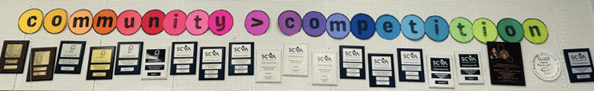 display of choir plaques with Community is greater than competition displayed above them in multi-colored circles for each letter and symbol