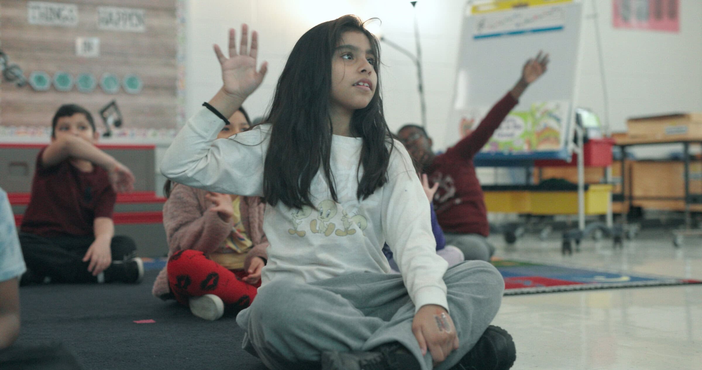 elementary music student sitting on classroom floor raising her hand