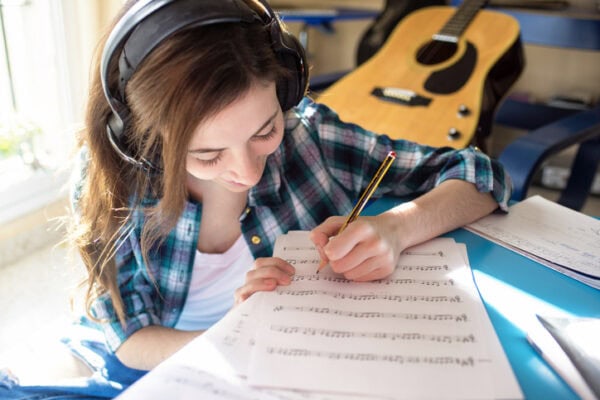 smiling guitar student wearing headphones marking sheet music