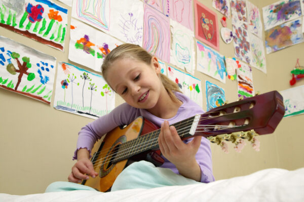Girl (5-7) playing acoustic guitar, low angle view
