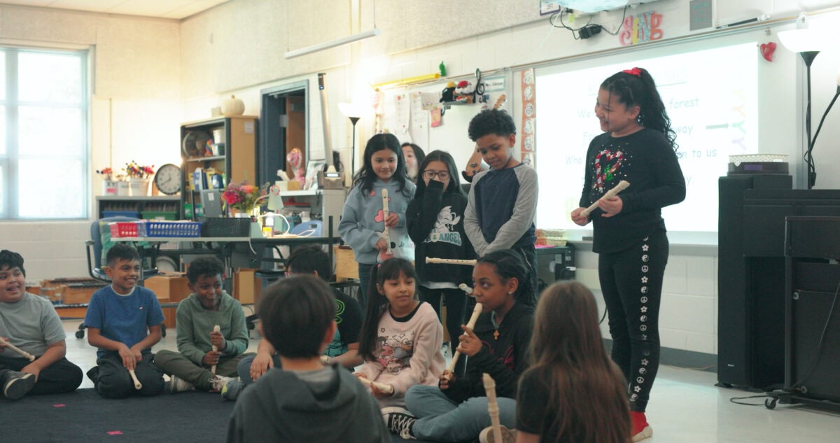 elementary music class sitting in a circle on the floor with recorders