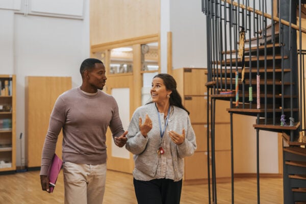 Smiling female teacher discussing with male colleague while walking in elementary school lobby