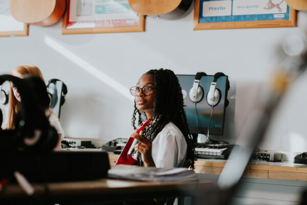 Student focuses on musical instrument during class in a music room with guitars and technology