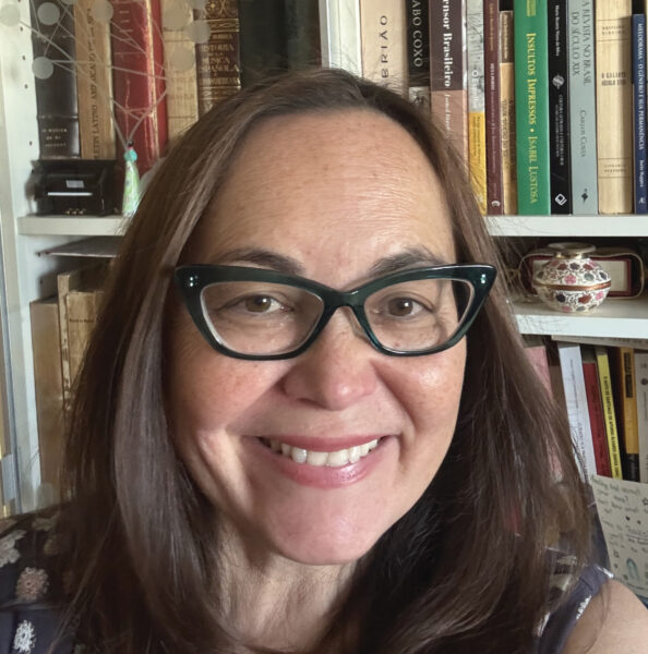 Beatriz Ilari headshot. Beatriz is wearing glasses and smiling at the camera with a bookcase behind her.
