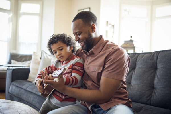 Father and son play a ukulele on the sofa