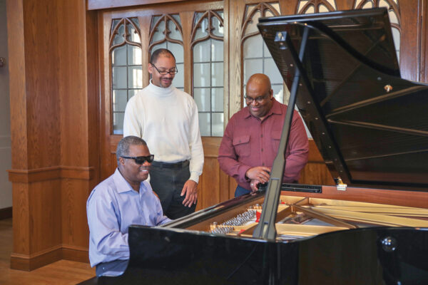 The Marcus Roberts Trio in a recital hall. Marcus Roberts on piano; Jason Marsalis, in the middle on drums; Rodney Jordan on bass.