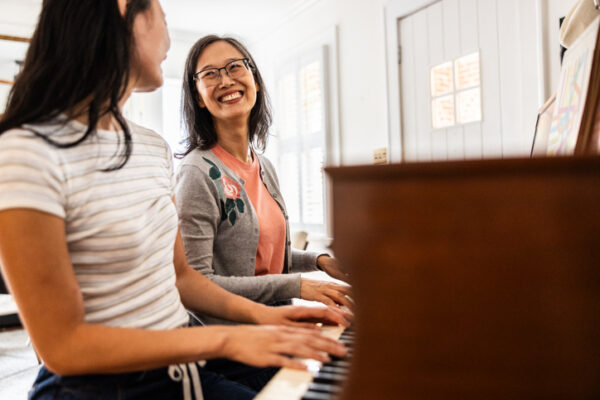smiling mother and daughter at piano at home