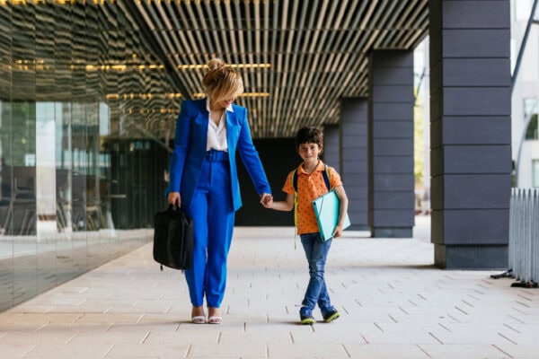 Business woman with briefcase bringing her son with her to work. Smiling boy happy to go with his mother to the office after school.