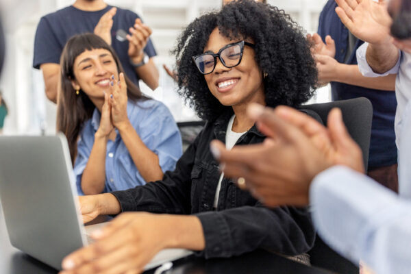 Excited team celebrates good news with colleague at desk in startup office