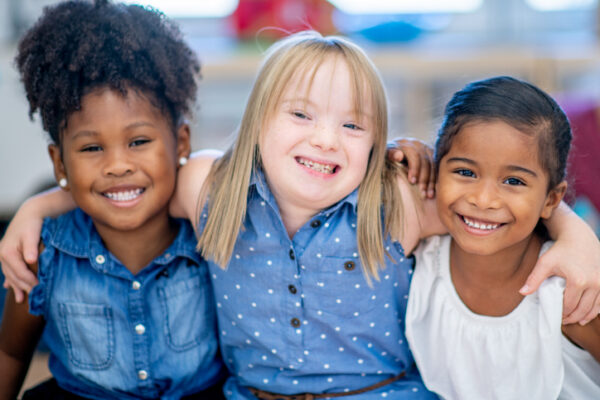 A group of three smiling elementary students sit side-by-side as they pose together for a portrait.