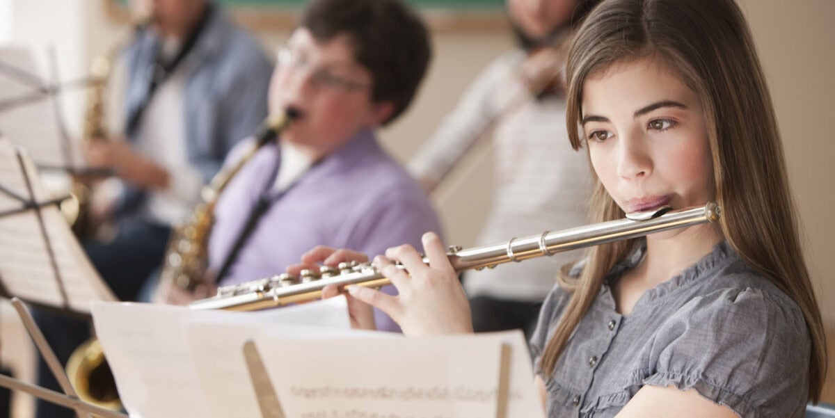 a middle school girl playing the flute in warm-ups with other students in the background