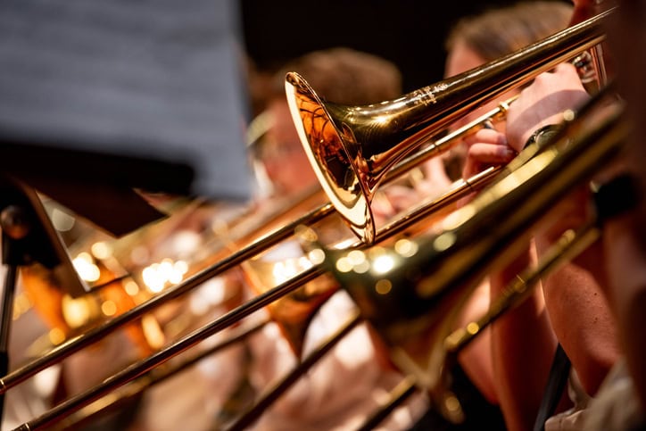 Close-up view of high school band students performing with brass instruments, including trumpets and trombones, during a school concert.