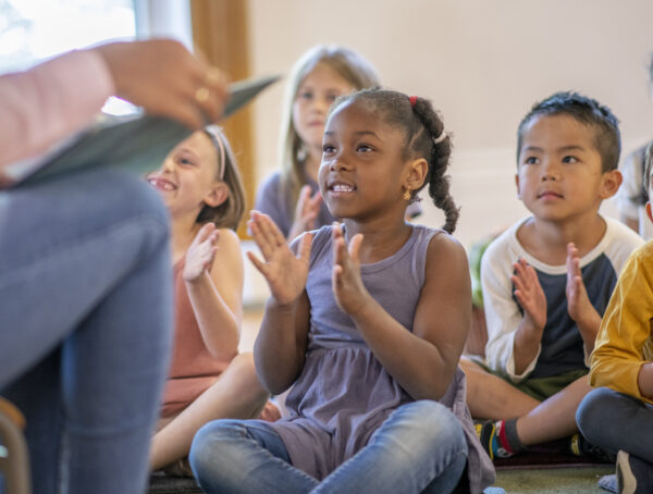 Diverse group of elementary students sitting in classroom clapping and singing