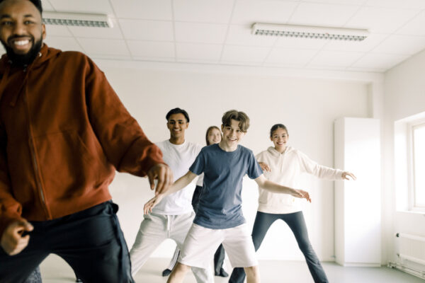 Smiling boy dancing with friends and teacher in studio at high school