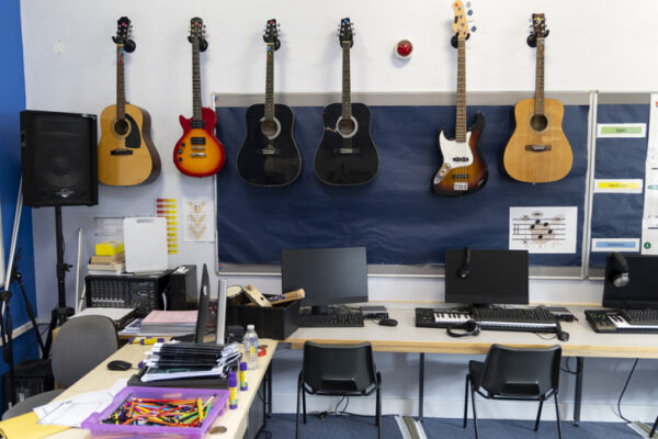 An empty high school music room ready with guitars on wall and laptops and school supplies on tables
