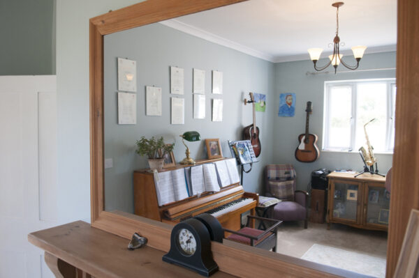 A general view looking through a mirror into a music room with Piano, guitars hanging on the wall and a saxophone by a window inside a home