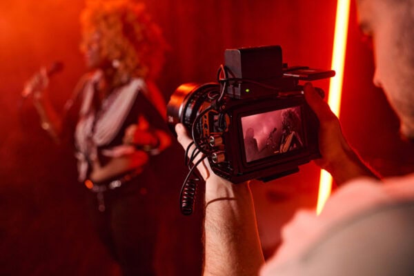 Close up of unrecognizable videographer holding camera and filming music video for jazz band