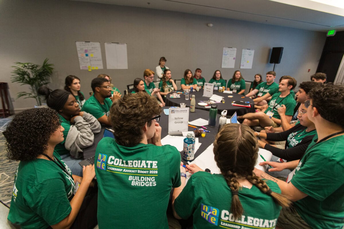 Large group of NAfME Collegiate members working around table wearing green tshirts with Building Bridges theme