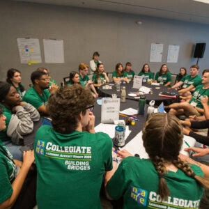 Large group of NAfME Collegiate members working around table wearing green tshirts with Building Bridges theme