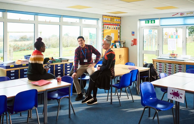 One male and two female teaching staff at work, discussing in school classroom, teamwork, strategy, support
