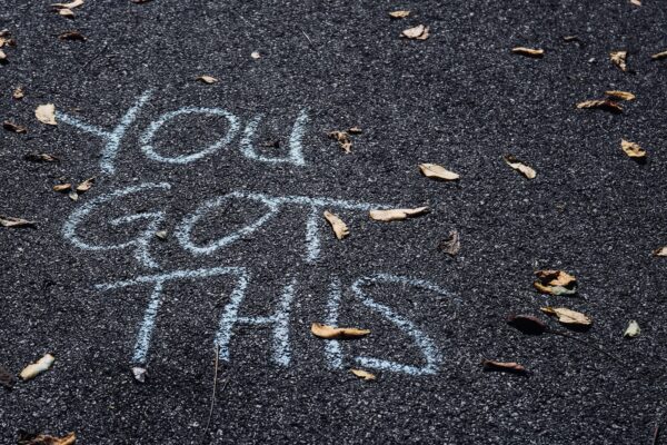 Phrase You Got This written in chalk on pavement with brown autumn leaves scattered around