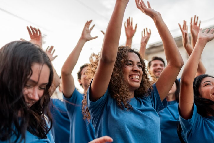 Volunteers in blue t-shirts celebrating with arms raised outdoors