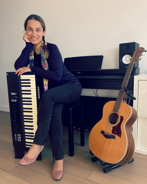 Laura Montanari smiling and sitting by a keyboard and guitar