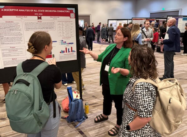 Attendees in front of a poster titled A Descriptive Analysis of All-State Orchestra Conductors 2015–2026 - Elizabeth A. Reed