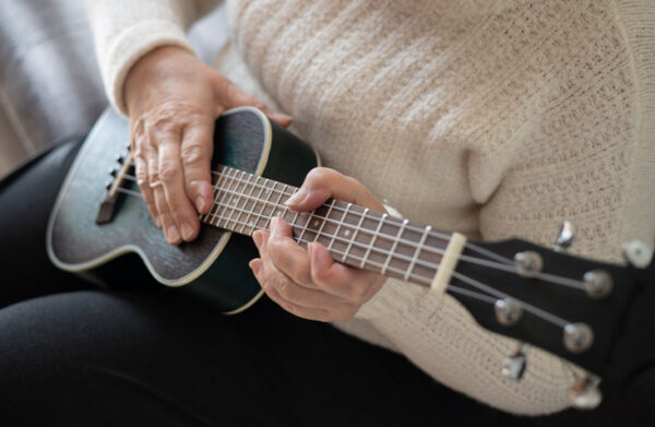 Hands of an elderly woman 70+ sitting on the sofa and playing the ukulele