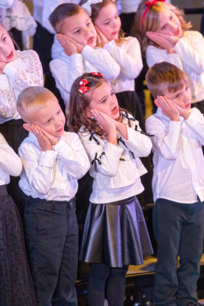 early childhood choir singing, wearing white attire on stage