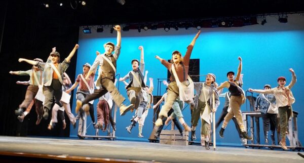 student theater production with cast dressed like newsies and jumping in the air