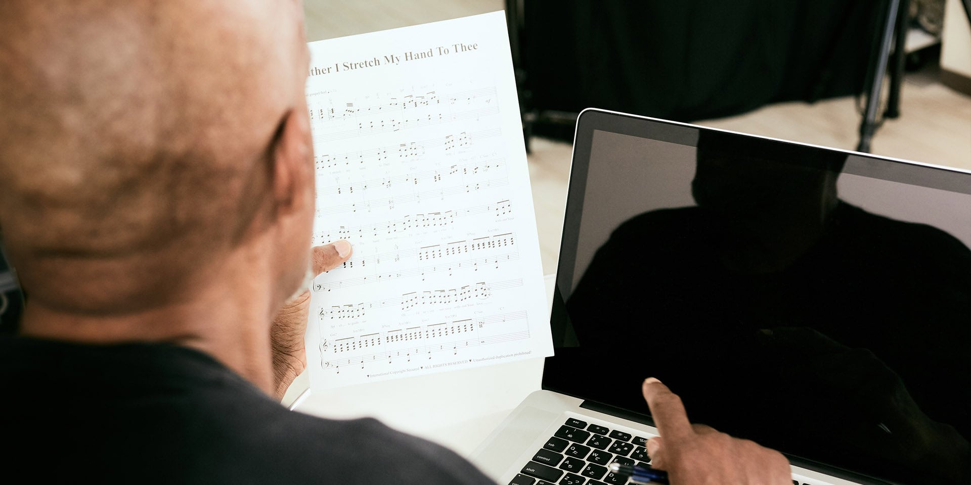 man reading sheet music along with a laptop