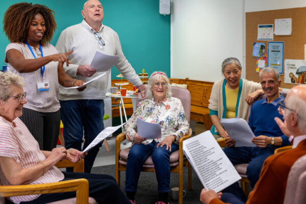 Senior citizens sitting in circle with caretaker singing and smiling