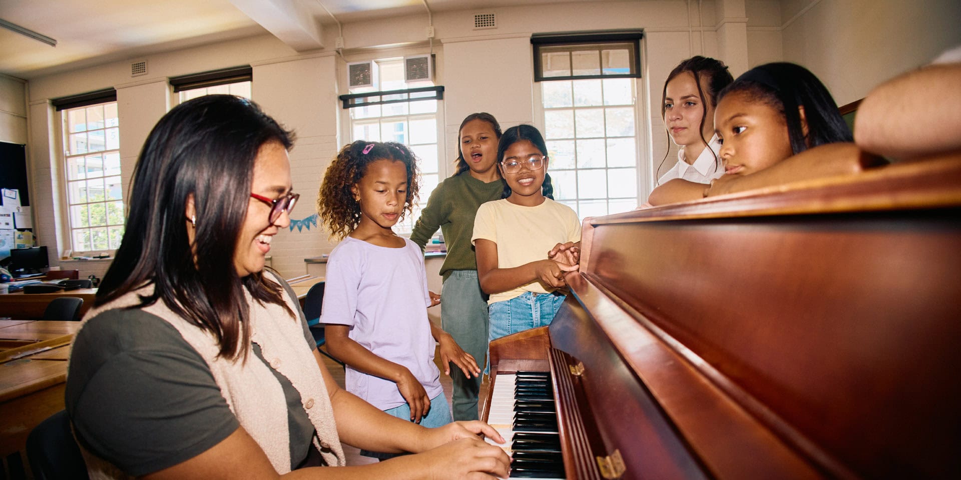 Music teacher and students singing around a piano