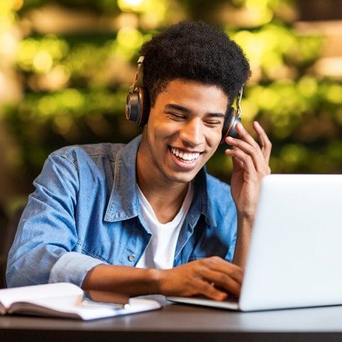 Cheerful teen guy with headset looking at laptop